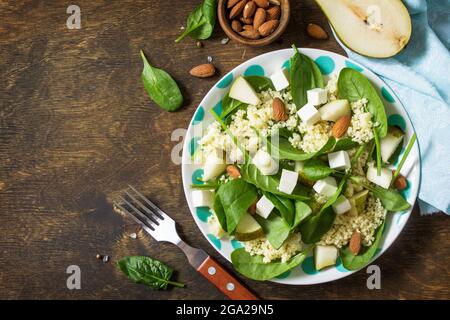 Autumn fruit salad. Couscous salad with pear, spinach, feta cheese and vinaigrette sauce on a wooden rustic table. Top view flat lay background. Copy Stock Photo