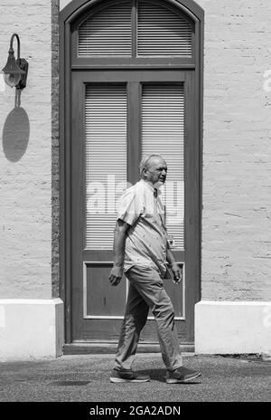 An old man walks on a sidewalk in the backgrounf of the door of the building. Black and white vintage style photo. Victoria, BC, Canada-July 23,2021. Stock Photo