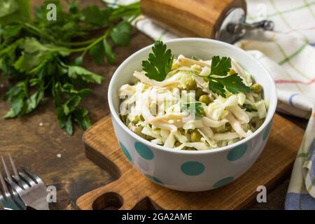Salad with fresh cabbage, calamary, cucumber and green peas in a bowl on a rustic table. Stock Photo