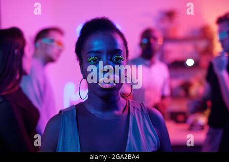 Happy young glamorous woman of African ethnicity in smart casualwear keeping eyes closed while standing in front of her dancing friends Stock Photo