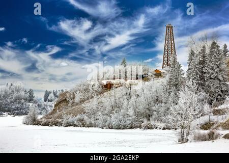 Old wooden oil rig on a hill along a shoreline with heavily frosted trees and dramatic clouds in a blue sky; Calgary, Alberta, Canada Stock Photo