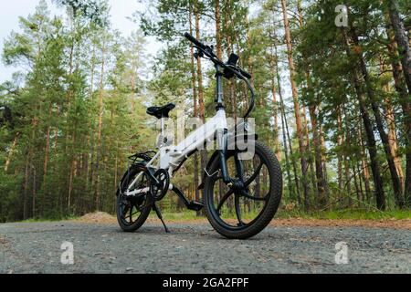 Eco friendly mode of transport. bicycle with an electric motor. An electric bike of white color on the background of a green forest. Stock Photo
