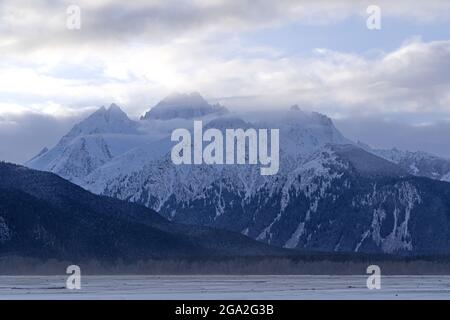 Misty clouds hovering around the snowcapped mountain peaks in the early morning light; Haines, Alaska, United States of America Stock Photo