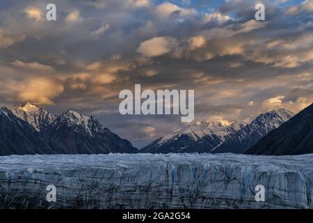 The vast Donjek Glacier in Kluane National Park with the sunset lighting up the clouds over the snowcapped mountaintops creating a stunning image, ... Stock Photo