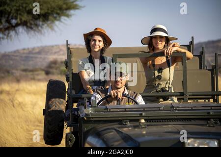 Women sitting in the back seat of a jeep on safari with a guide driving them through the savanna, looking at camera at the Gabus Game Ranch Stock Photo