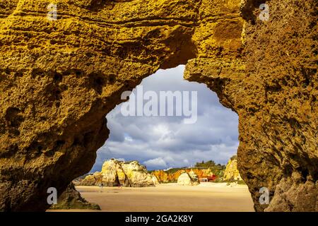 Looking through the detail of a sea arch on Dona Ana Beach at low tide with its sunlit shoreline and sandstone sea stacks along the famous Algarve ... Stock Photo