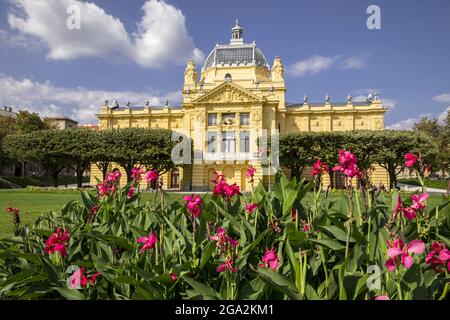 Colorful flower bed in front of the yellow stone facade of the Art Pavilion in Zagreb on the Lenuci Horseshoe, Lower Town area at King Tomislav Square Stock Photo