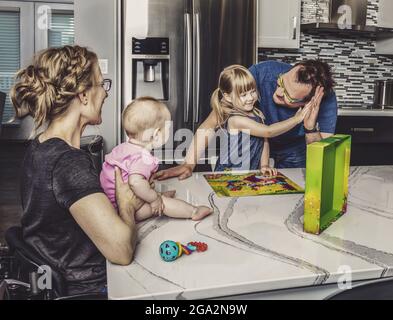 A paraplegic mother and her family making a puzzle and spending quality time together in their kitchen; Edmonton, Alberta, Canada Stock Photo