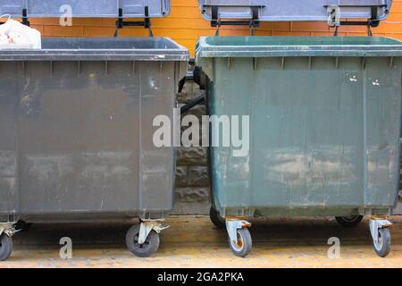 https://l450v.alamy.com/450v/2ga2pka/plastic-large-trash-cans-with-the-lids-up-and-garbage-inside-against-a-brick-orange-wall-big-green-and-grey-plastic-dumpsters-on-a-city-street-waste-2ga2pka.jpg
