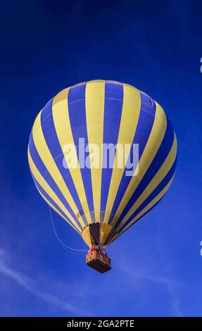 Yellow and blue striped hot air balloon in mid-flight against a blue sky; Phoenix, Arizona, Untied States of America Stock Photo