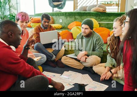 Group of intercultural financial managers brainstorming and discussing papers with graphs and charts at working meeting on the floor Stock Photo