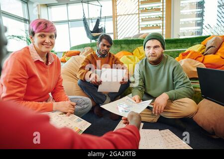 One of several young intercultural financial managers pointing at diagram on paper while explaining data to colleagues at working meeting Stock Photo
