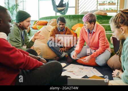 One of several young intercultural financial managers pointing at diagram on paper while explaining data to colleagues at working meeting Stock Photo