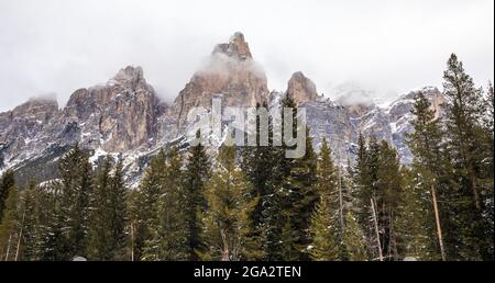 The jagged mountaintops of the Dolomites rising up from the pine tree forest in the Alta Badia Region on a wintry day; South Tyrol, Italy Stock Photo