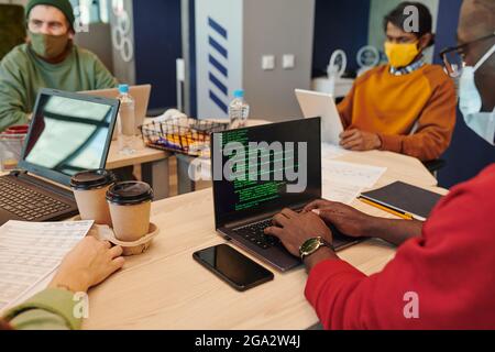 Smiling young businesswoman on laptop display looking at male colleague sitting by desk in open space office during video communication Stock Photo