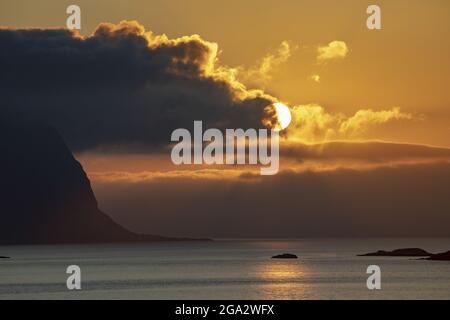 Midnight Sun glowing from behind the clouds and reflecting on the North Atlantic Ocean; Lofoten, Arctic Circle, Norway Stock Photo