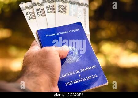 In this photo illustration, a man displays his Work and Social Security Card of Brazil with two hundred reals bills.It is the document that guarantees access to the rights of the Brazilian worker. Stock Photo