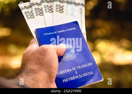 Brazil. 28th July, 2021. In this photo illustration, a man displays his Work and Social Security Card of Brazil with two hundred reals bills.It is the document that guarantees access to the rights of the Brazilian worker. (Credit Image: © Rafael Henrique/SOPA Images via ZUMA Press Wire) Stock Photo