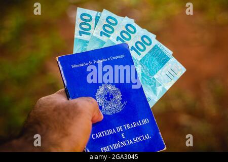Brazil. 28th July, 2021. In this photo illustration, a man displays his Work and Social Security Card of Brazil with one hundred reals bills.It is the document that guarantees access to the rights of the Brazilian worker. (Credit Image: © Rafael Henrique/SOPA Images via ZUMA Press Wire) Stock Photo