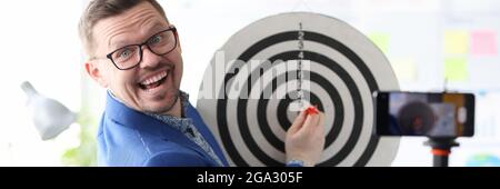 Businessman playing darts in front of mobile phone camera Stock Photo