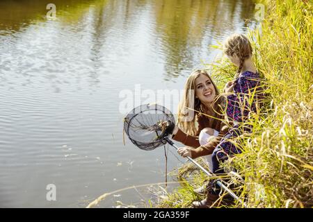 A mother spending quality time outdoors with her daughter and using a net to catch bugs in a stream at a city park; Edmonton, Alberta, Canada Stock Photo
