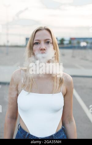 Blonde woman in city with electronic cigar vaping Stock Photo
