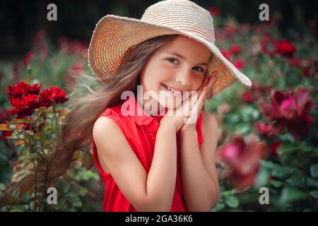 Beautiful little girl in roses garden in park. Charming woman smiling outdoor with flowers. Stock Photo