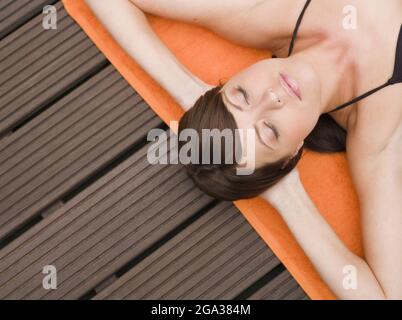 Young woman lounging on a towel on the deck; Germany Stock Photo