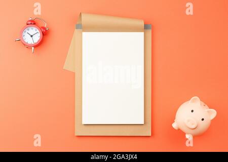 Notepad with red alarm clock and pig piggy bank. Stock Photo