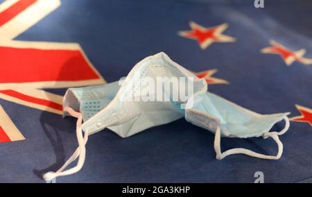 A discarded personal face mask protecting the wearer from coronavirus laying crumpled on a closeup of the New Zealand national flag. Covid Eliminated Stock Photo