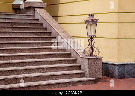 marble staircase with stone steps and iron forged lantern in a retro style on the corner of a house with a granite plinth, close-up of the architectur Stock Photo