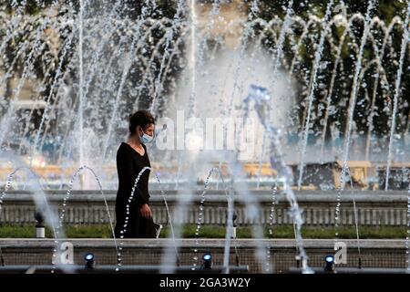 Bucharest, Romania. 28th July, 2021. A woman walks past a fountain during a hot day in downtown Bucharest, Romania, on July 28, 2021. Romanian authorities issued an orange code, announcing a heatwave with temperatures reaching 40 degrees in the south of the Balkan country in the next few days. Credit: Cristian Cristel/Xinhua/Alamy Live News Stock Photo