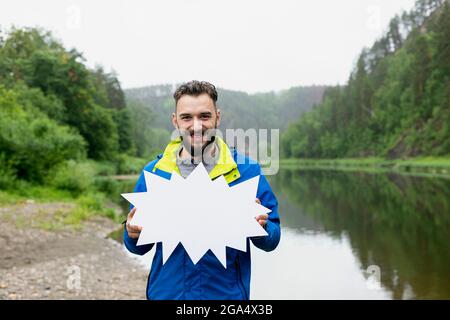 Smiling young man with beard in jacket says any words with possibility of writing them on white star background, which he holds in front of him agains Stock Photo
