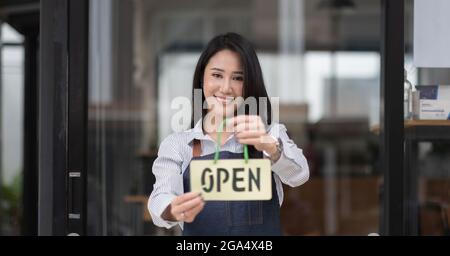 Startup successful small business owner sme beauty girl stand hand hold open sign coffee shop or restaurant. Portrait of young asian woman barista Stock Photo