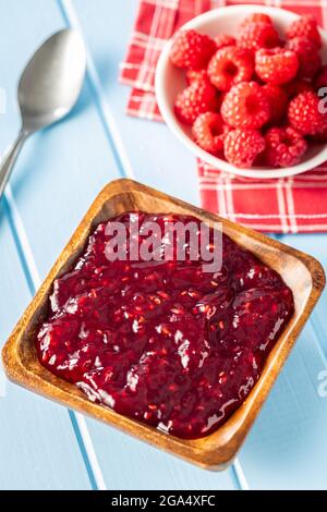 Red rasberries jam in bowl and ripe raspberries on blue table. Stock Photo