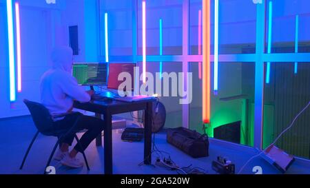 Hacker working place: hacker working in a room with colored neon lights. He writing hacker program. Stock Photo