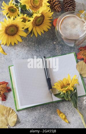 Good Morning. To do list concept. A bouquet of large sunflowers, coffee cup and empty notebook on a stone table. Stock Photo