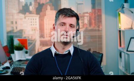 Portrait of caucasian young man talking to the camera in a call center. There are skyscrapers in the background. Stock Photo