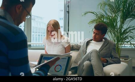 Group of diverse men and woman sharing papers and working with laptop in modern office having meeting Stock Photo