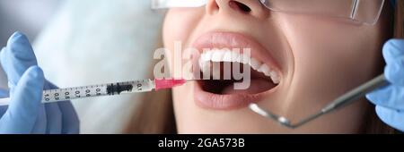 Dentist making injection in gum of female patient in clinic Stock Photo