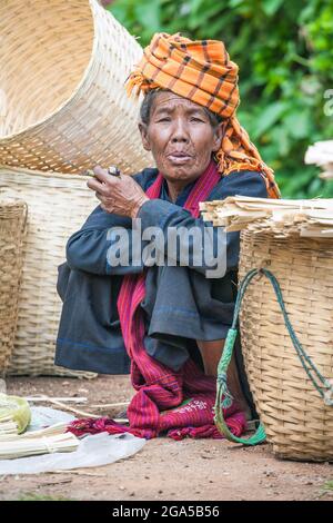 Market trader from Pa'o (Pa-o) ethnic hill tribe wearing orange turban smoking cigar selling vegetables in Kalaw, Shan State, Myanmar Stock Photo