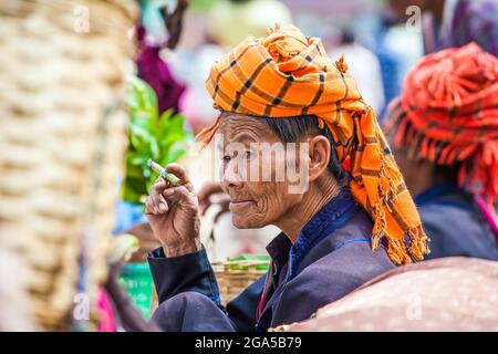 Market trader from Pa'o (Pa-o) ethnic hill tribe wearing orange turban smokes cigar selling vegetables in Kalaw, Shan State, Myanmar Stock Photo