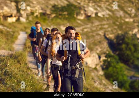 Group of young tourists hikers walking along mountain valley during traveling Stock Photo