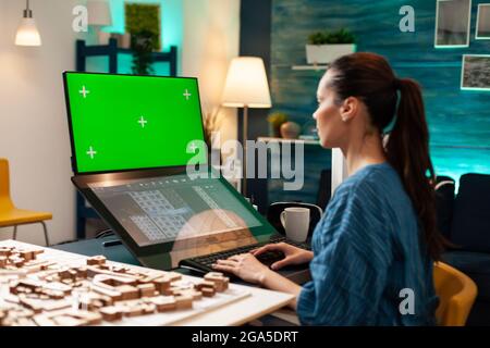 Engineer architect using green screen and blueprint on monitor computer screen at workplace. Woman doing manufacturing work on software template for chroma key mockup development project Stock Photo
