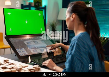 Tehnician woman working on touchpad monitor for design using green screen chroma key mockup isolated background and building plan. Construction expert doing development innovation model Stock Photo