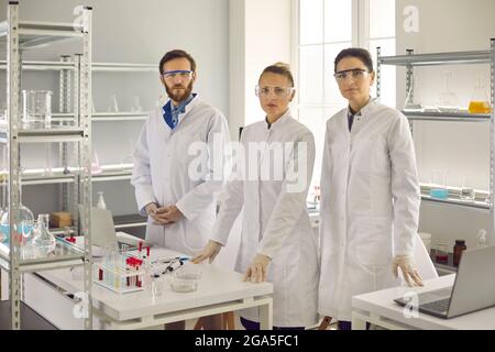 Group portrait of young medical scientists in lab coats and goggles standing in laboratory Stock Photo