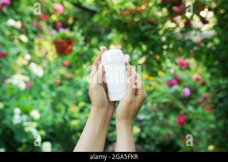 Hands holding natural deodorant on green flowers background. Zero waste concept Stock Photo