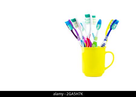 Several old toothbrushes are housed in a yellow plastic tumbler isolated on white background. Stock Photo