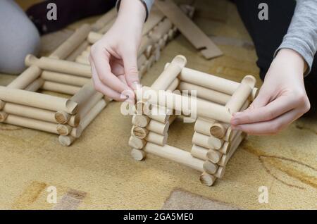 Girl builds a hut from wooden logs, children's wooden constructor Stock Photo