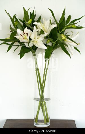 Vertical shot of a bouquet of lilies in a tall glass vase indoors Stock Photo
